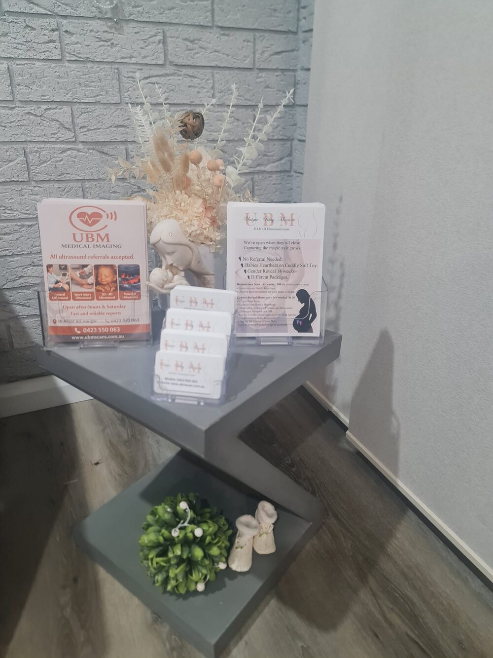 A display shelf at the UBM Scans clinic holding keepsake cards, price lists and a dried flower arrangement