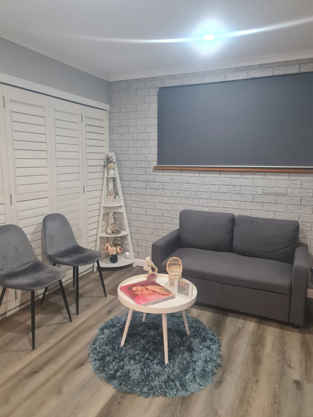 The UBM Scans waiting area: a grey sofa and two chairs around a small round table on a pale rug, beside a white-brick wall