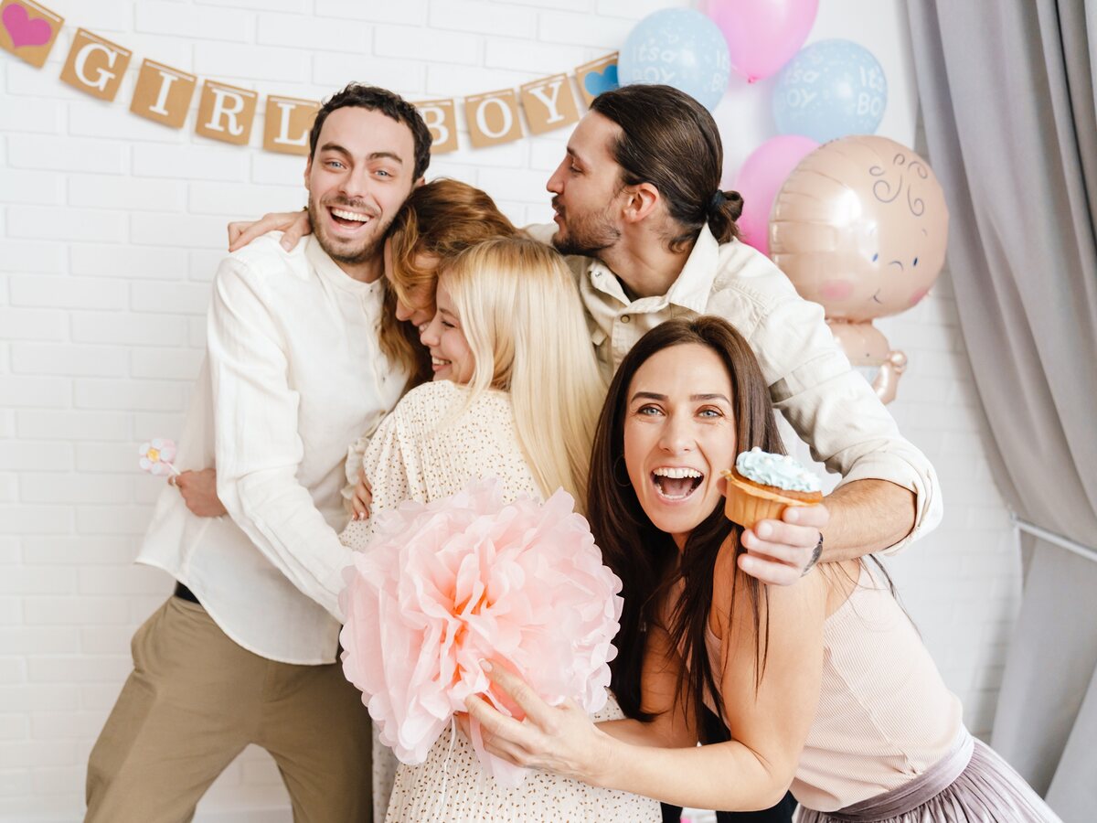 A family celebrating a gender reveal beneath girl and boy bunting, with pink and blue balloons