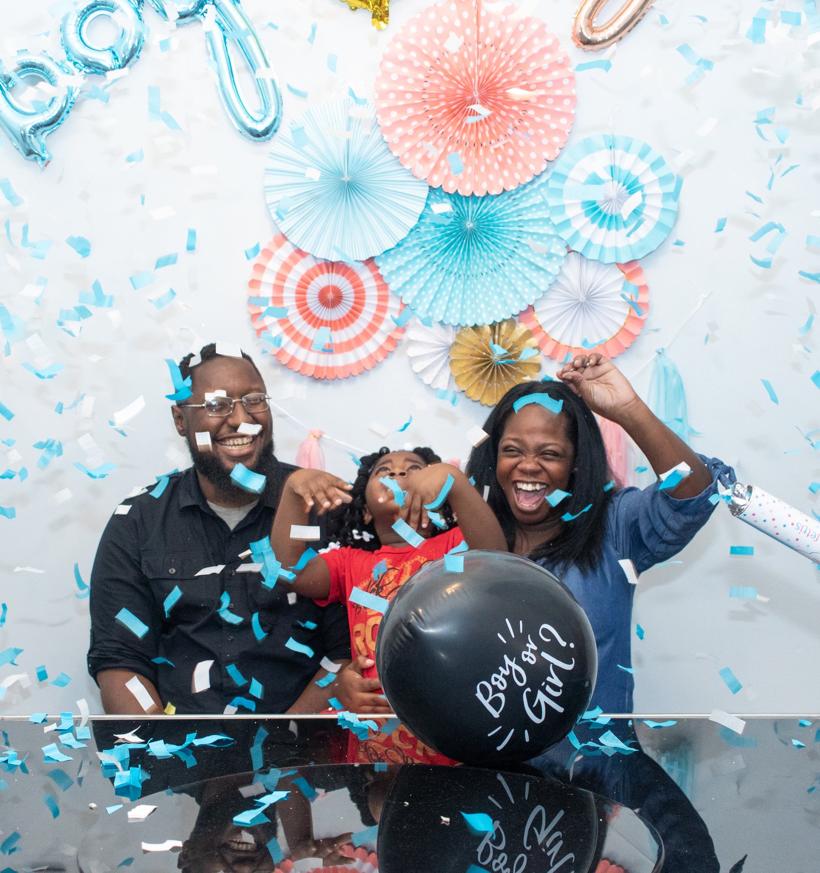 Parents celebrating their baby's gender reveal with confetti and a balloon