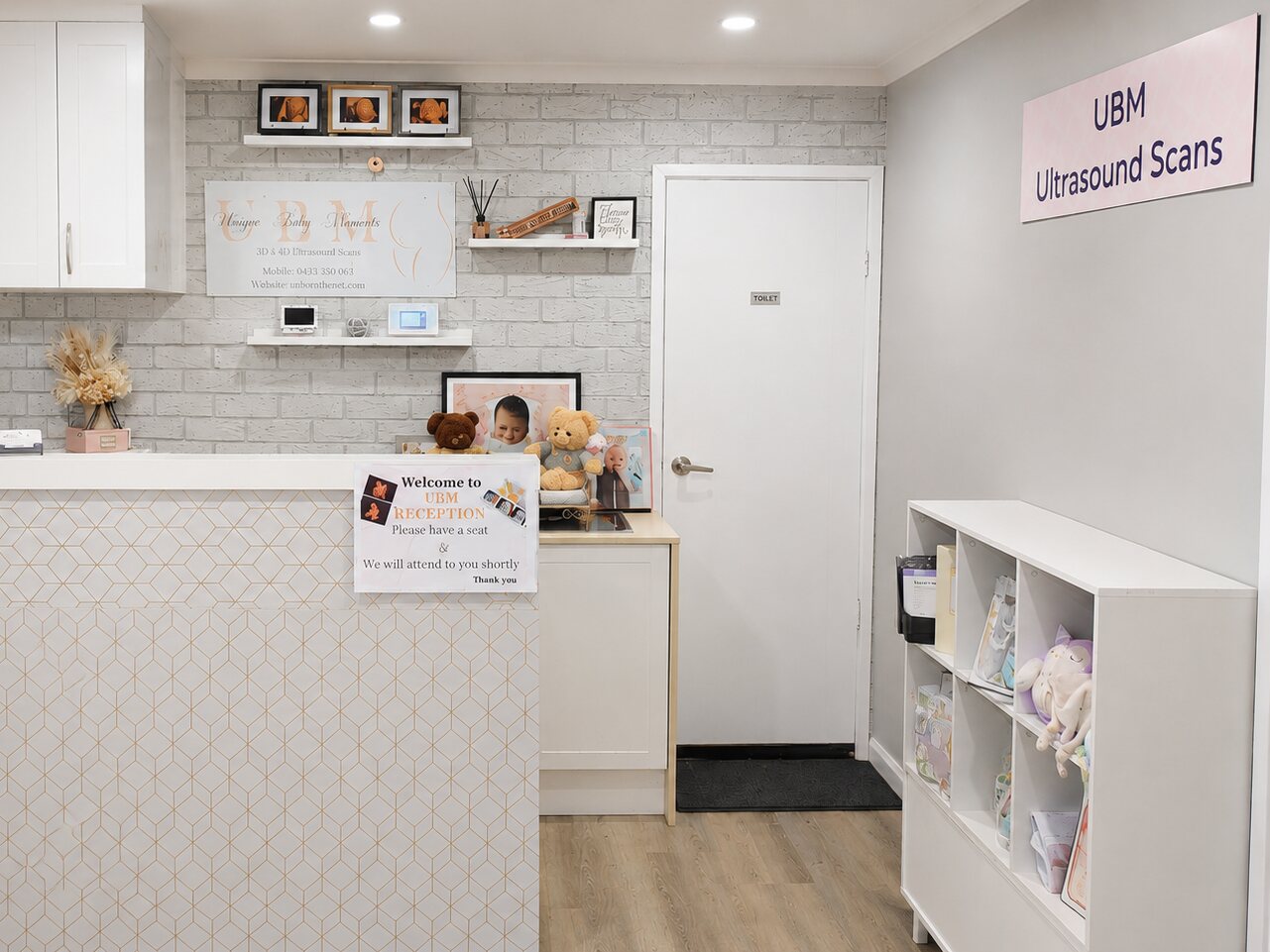 The UBM Scans reception in Menai: a tiled front desk beneath the Unique Baby Moments sign, with scan prints framed on the brick wall and a shelf of keepsakes beside the waiting area